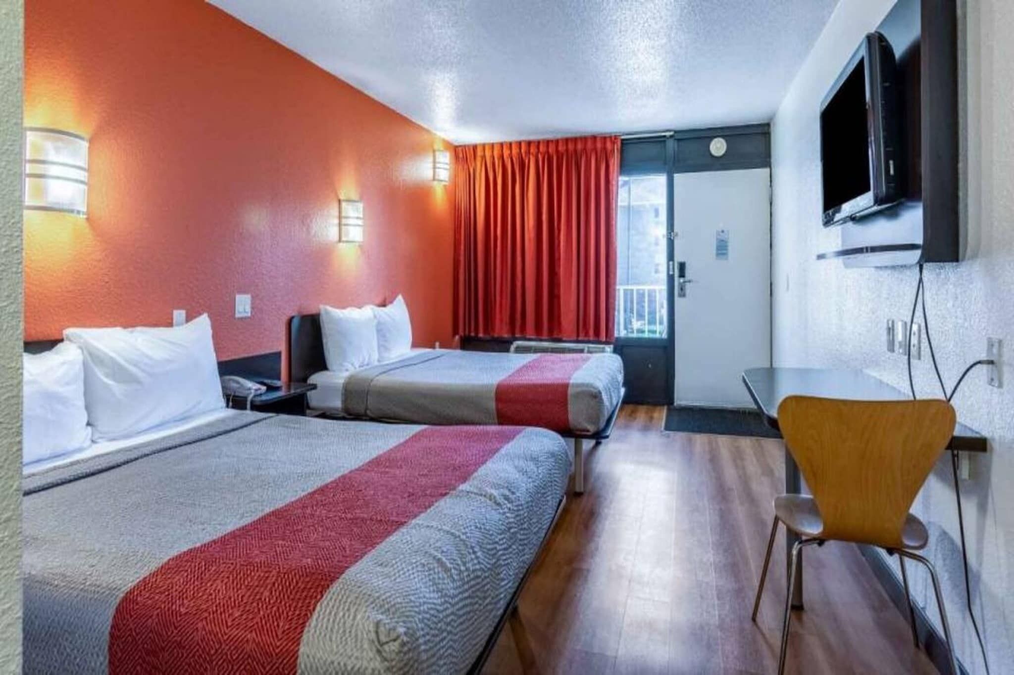 A hotel room with two beds, a desk, a chair, a TV, and a window with curtains.