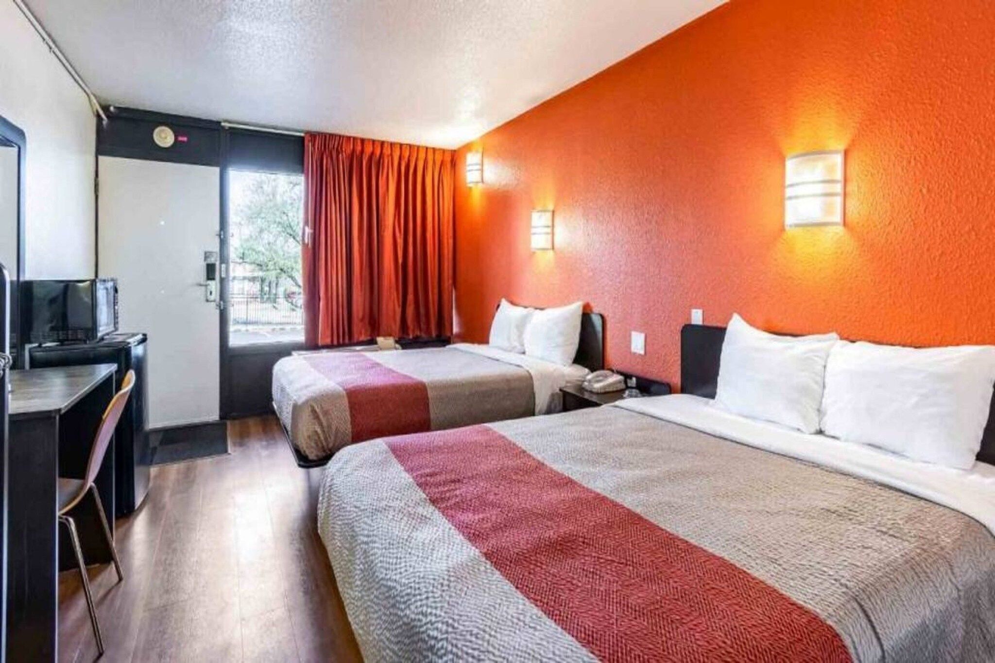 A hotel room with two beds, a desk, a television, and a window with curtains.