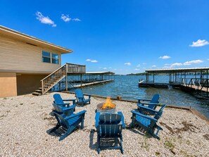 A waterfront property with a fire pit and Adirondack chairs.