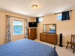 A bedroom with a bed, dresser, TV, and a view of a body of water through a window.