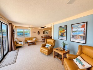 A spacious living room with a large window, a ceiling fan, and a dining area with a view of the outdoors. - Waters Edge Lakefront Escape (Gravois Mills)