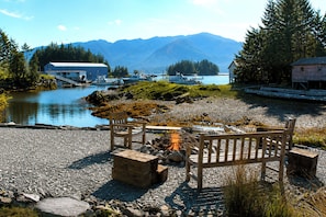 A lakeside setting with a wooden bench, a fire pit, and boats docked near a dock.