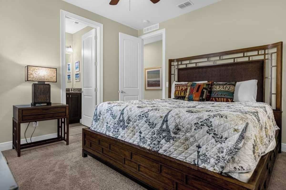A bedroom with a bed, a nightstand, a lamp, and a door leading to another room.