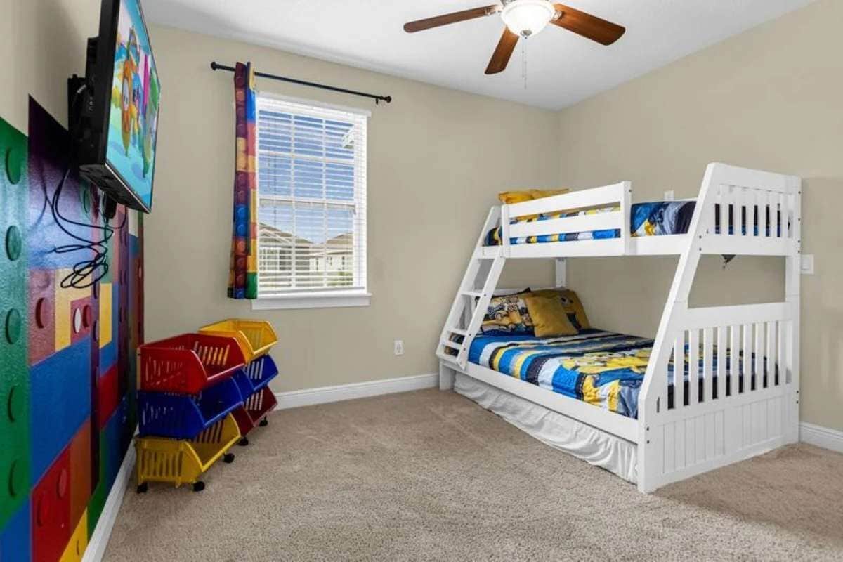 A child's bedroom with bunk beds, a ceiling fan, a window with blinds, and colorful storage bins.