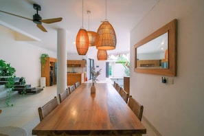 Uma sala de jantar espaçosa com uma longa mesa de madeira, luminárias pendentes de vime e um espelho grande na parede.