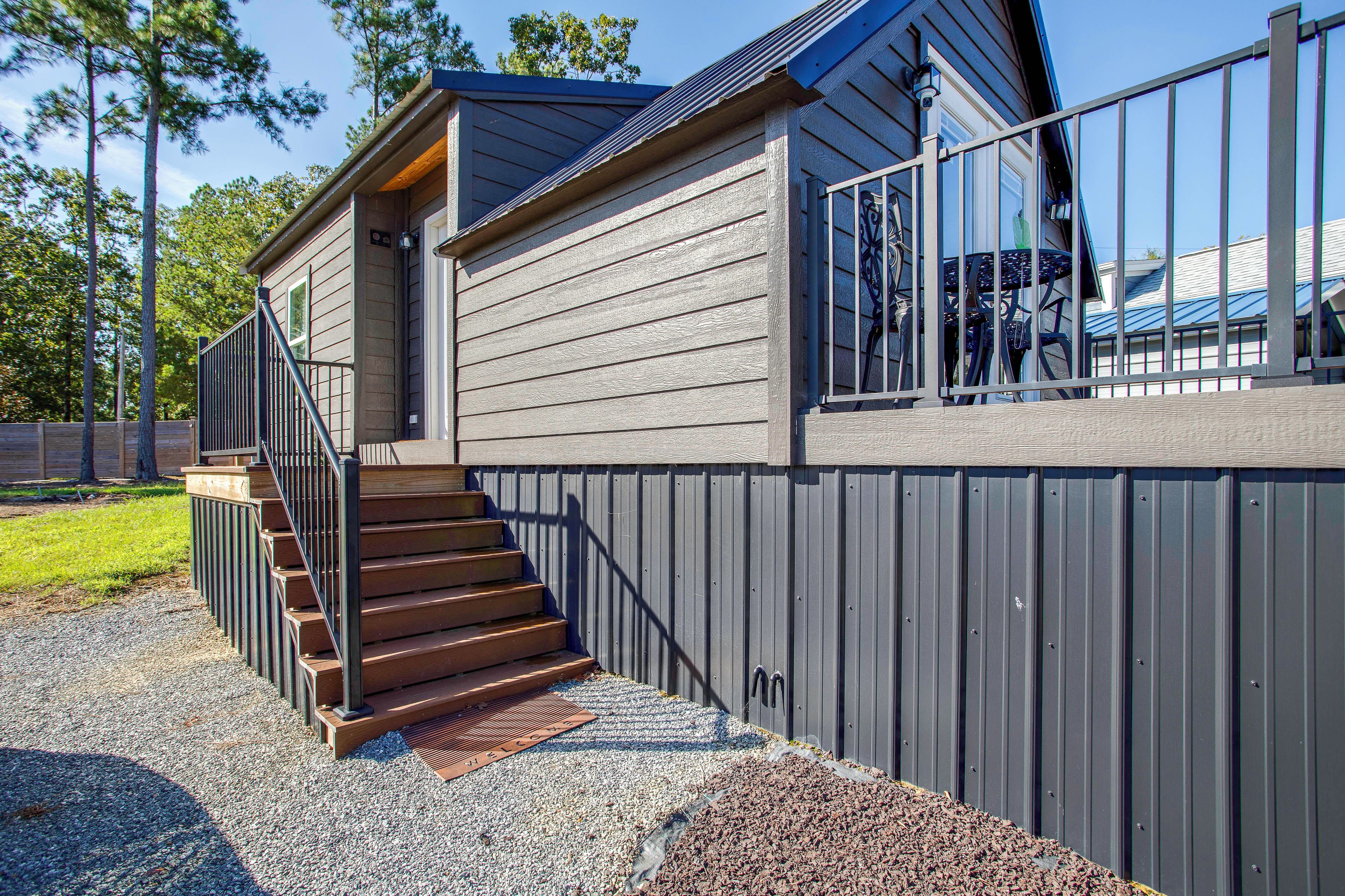 A two-story building with a wooden staircase leading to the entrance, a metal fence, and a gravel driveway.