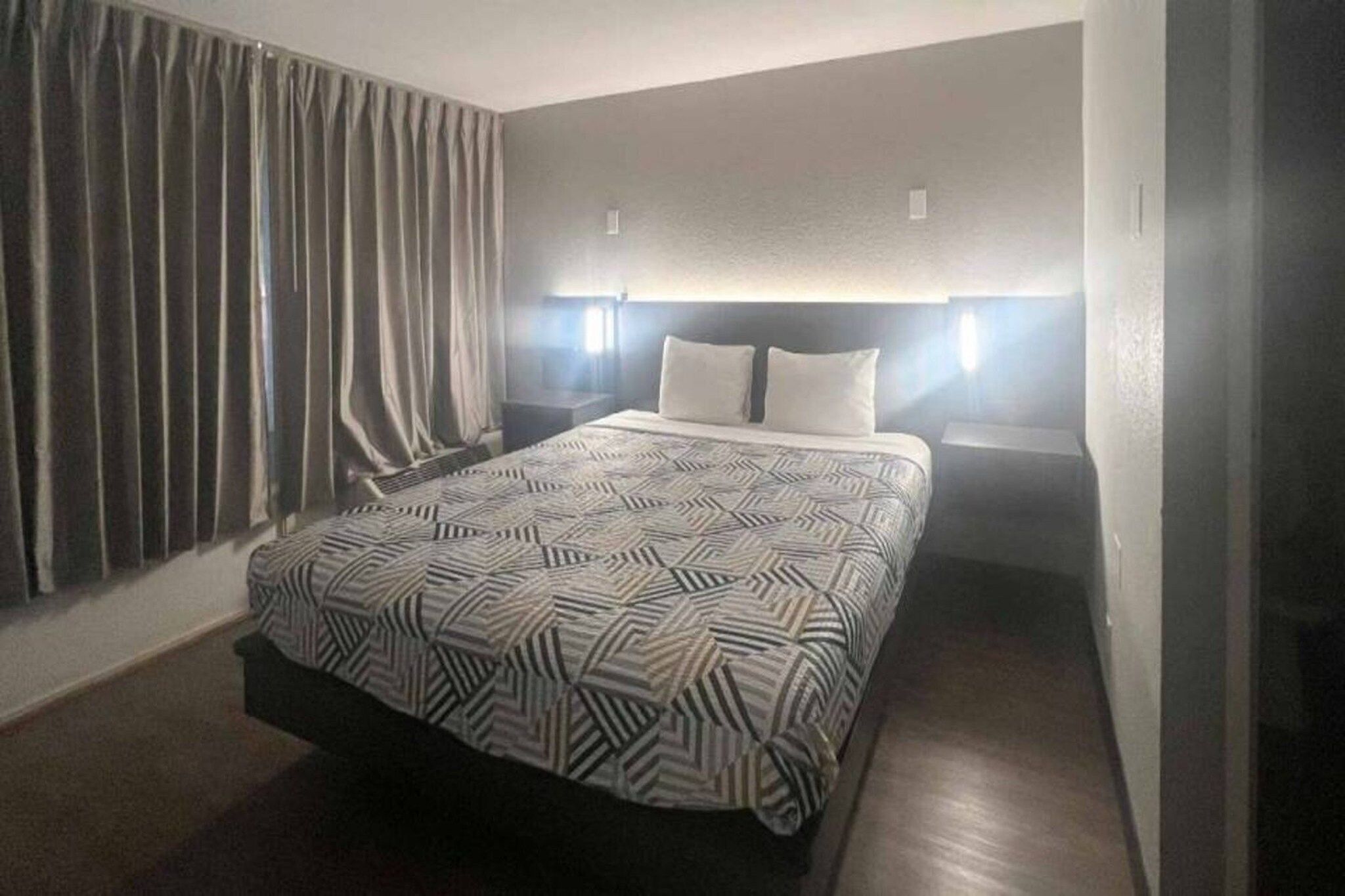 A hotel room with a bed, curtains, and bedside lamps.