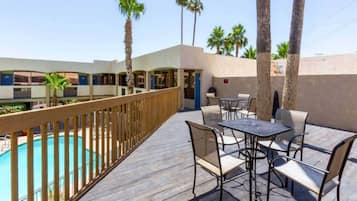 A poolside area with a wooden deck, outdoor seating, and a view of a building with multiple windows.