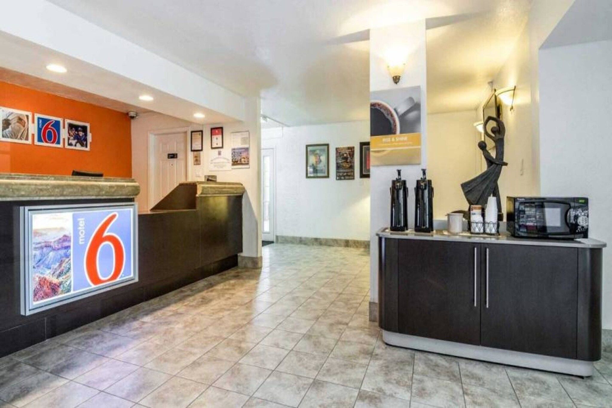 A hotel lobby with a reception desk, a large number '6' sign, a coffee station, and a statue.