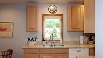 A kitchen with wooden cabinets, a built-in dishwasher, a sink with a faucet, and a window with a view of greenery.