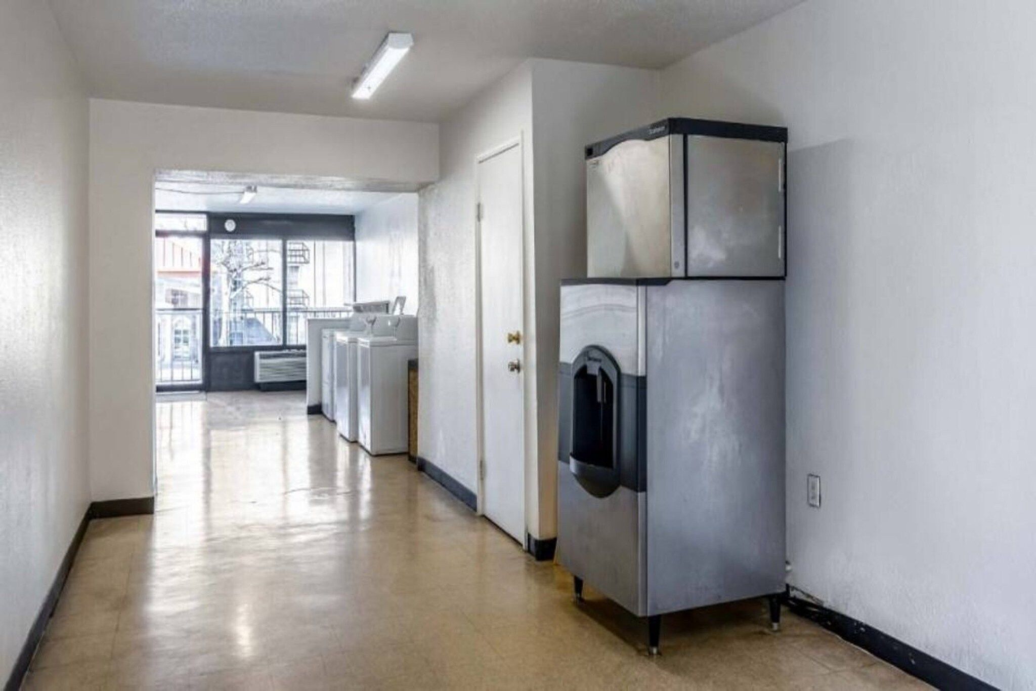 A laundry room with a large industrial washer and dryer, a door leading to another room, and a view of the outside through a window.
