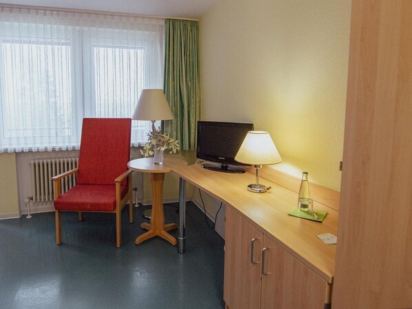 A hotel room with a red chair, a small round table with a lamp, a television, and a cabinet. - defaultName (Falkenstein/Vogtland)