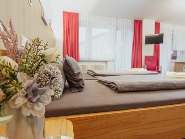 A hotel room with a bed, a bedside table, a vase with flowers, and a window with curtains. - defaultName (Falkenstein/Vogtland)