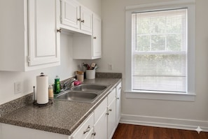 A kitchen with white cabinets, a granite countertop, a double sink, and a window with blinds. - Modern Houston Heights Gem - Stylish & Spacious (Houston)