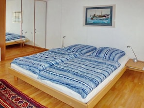 Ein Schlafzimmer mit einem hölzernen Bett, einem Spiegel, einem gerahmten Bild an der Wand und einem gemusterten Teppich.