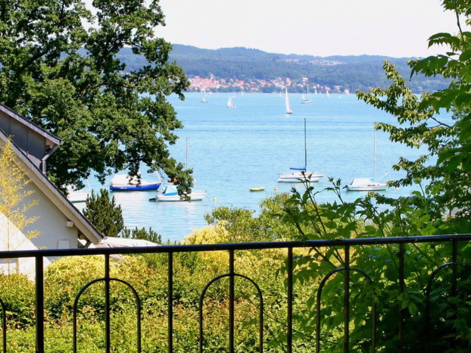 Blick auf einen See mit Booten, umgeben von Bäumen und einer in der Ferne liegenden Stadt.