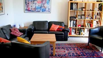 A living room with two black leather sofas, a wooden coffee table, a colorful rug, and a bookshelf filled with books and decorative items.