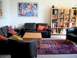 A living room with two black leather sofas, a wooden coffee table, a colorful rug, and a bookshelf filled with books and decorative items.