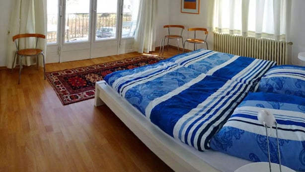Un dormitorio con una cama, dos sillas, un radiador y una ventana con cortinas.