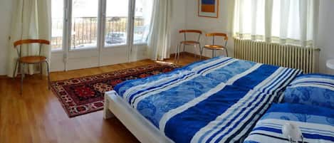 Un dormitorio con una cama, dos sillas, un radiador y una ventana con cortinas.