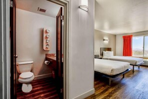 Ett hotellrum med trägolv, en säng, ett skrivbord och ett fönster med röda gardiner.