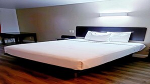 Hotellihuone, jossa on suuri sänky, yöpöytä, yövalaisin ja seinään kiinnitetty valaisin.