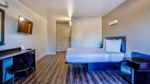 A hotel room with a bed, desk, chair, and a television on the wall. - 1 Queen Bed | Non-Smoking (Hesperia)