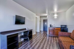 Ein Hotelzimmer mit Schreibtisch, Stuhl, Fernseher, Küchenzeile und einem gemusterten Sofa.