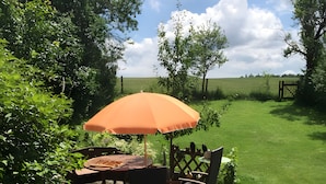 An outdoor patio area with a table and chairs under an umbrella, surrounded by greenery and a view of the countryside. - Apartment 'Ferienwohnung in Upflamör' with Shared Garden, Balcony and Wi-Fi (Zwiefalten)