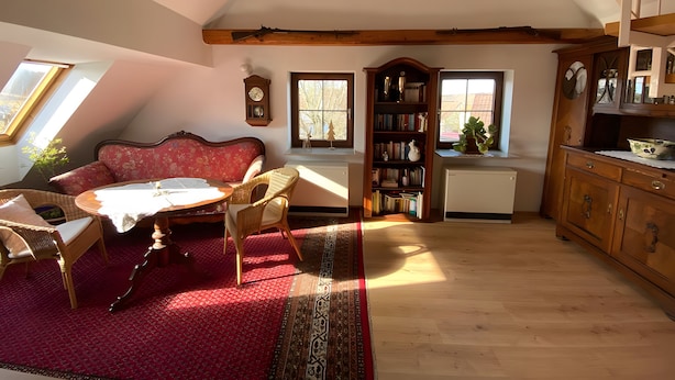 A cozy living room with a red sofa, a wooden coffee table, a bookshelf, and a dining area with a table and chairs. - Apartment 'Ferienwohnung in Upflamör' with Shared Garden, Balcony and Wi-Fi (Zwiefalten)