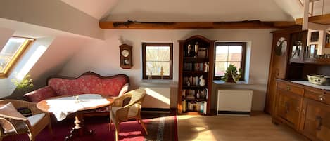 Una sala de estar acogedora con un sofá rojo, una mesa de centro de madera, una estantería y un comedor con mesa y sillas.