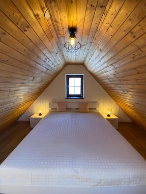 A bedroom with a sloped ceiling, a window, two bedside tables with lamps, and a bed with a white mattress. - Apartment 'Ferienwohnung in Upflamör' with Shared Garden, Balcony and Wi-Fi (Zwiefalten)