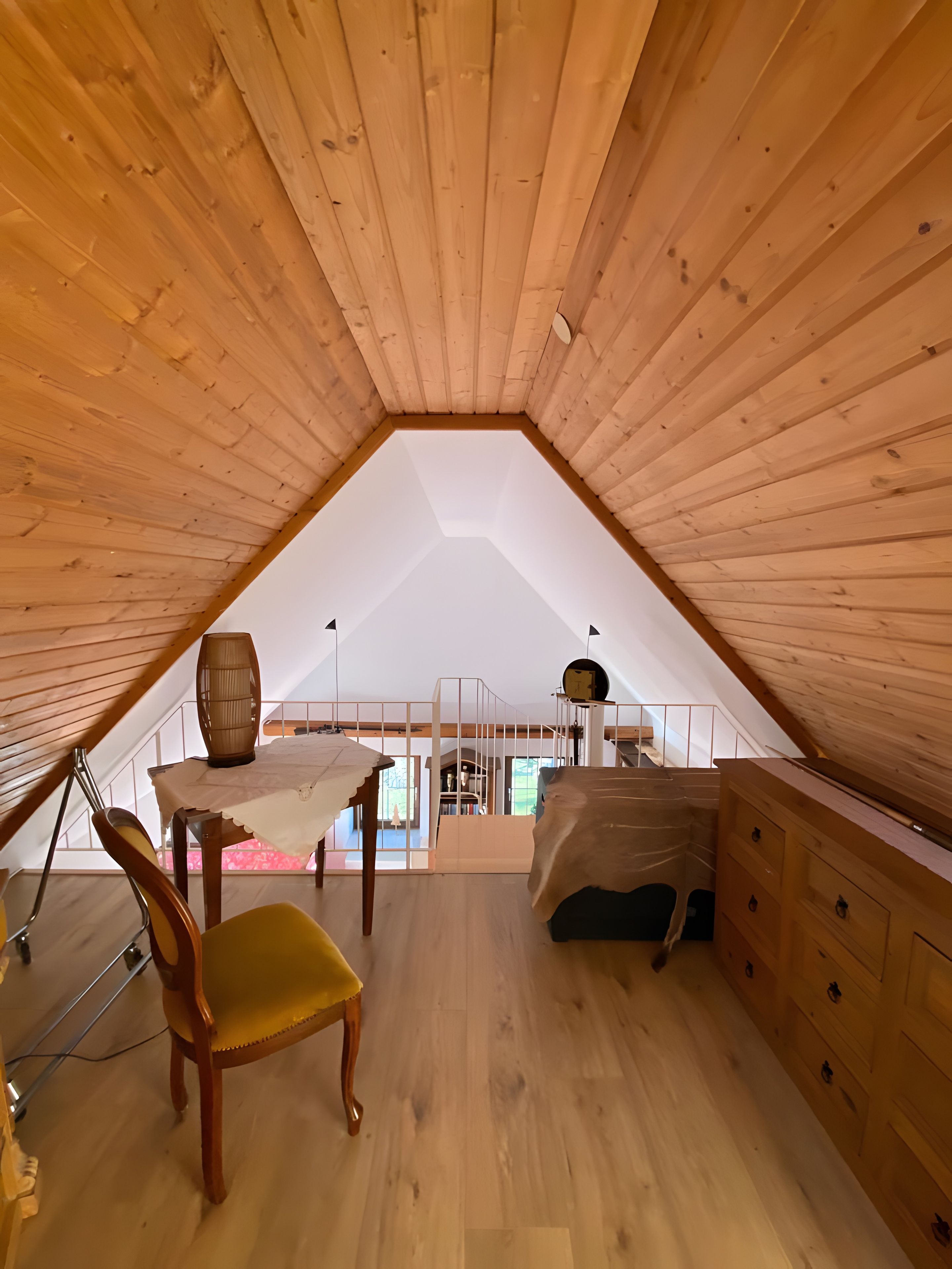 Een houten interieur met een schuine kap, een tafel met een vaas, een stoel en een dressoir.