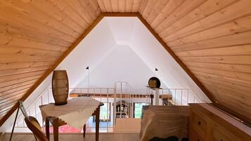 Een houten interieur met een schuine kap, een tafel met een vaas, een stoel en een dressoir.
