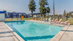 Ein Pool mit Liegestühlen und einem umzäunten Bereich, umgeben von Gebäuden und Bäumen.