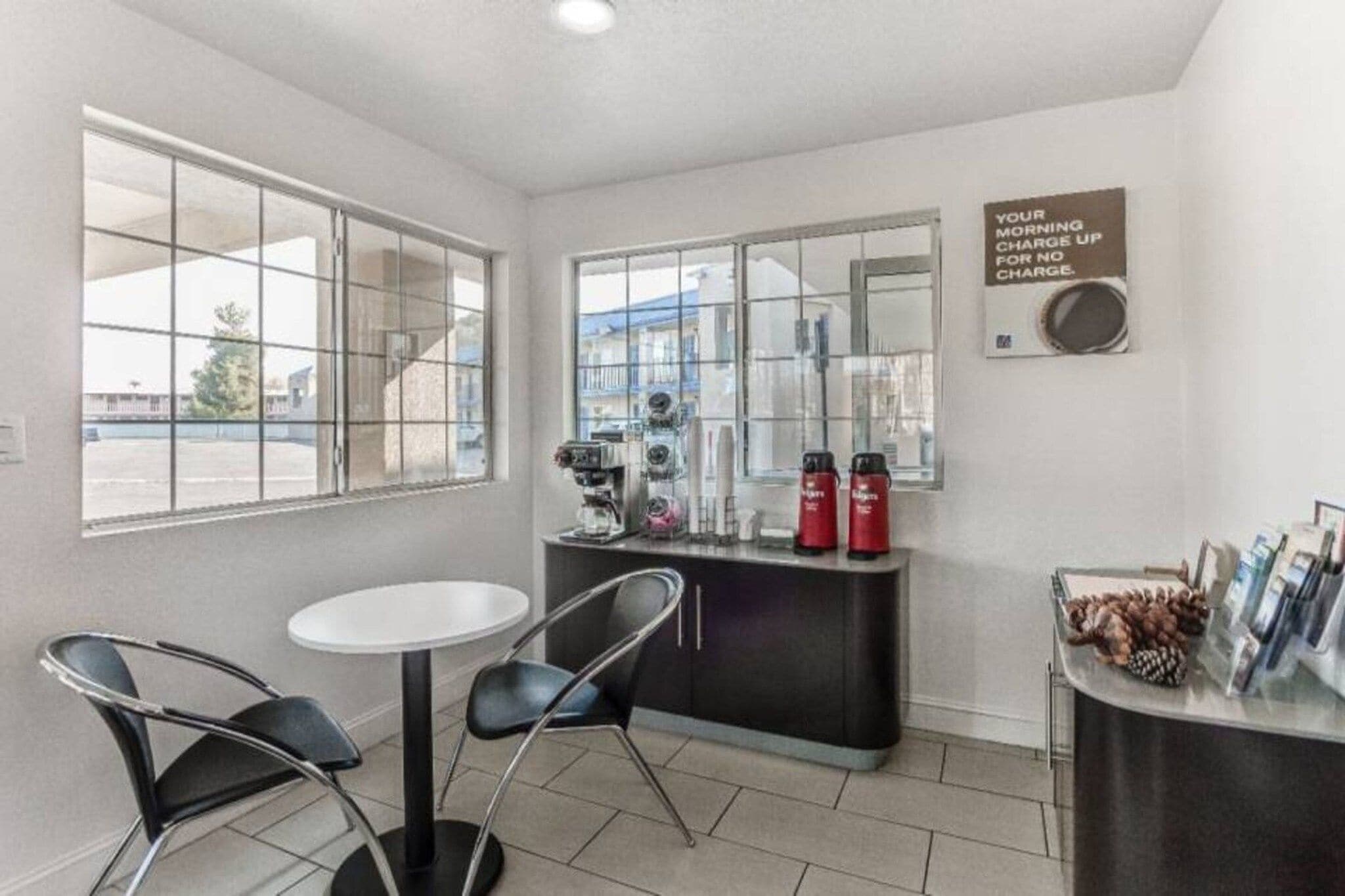 A small room with a white table and two chairs, a coffee machine, and a sign on the wall.