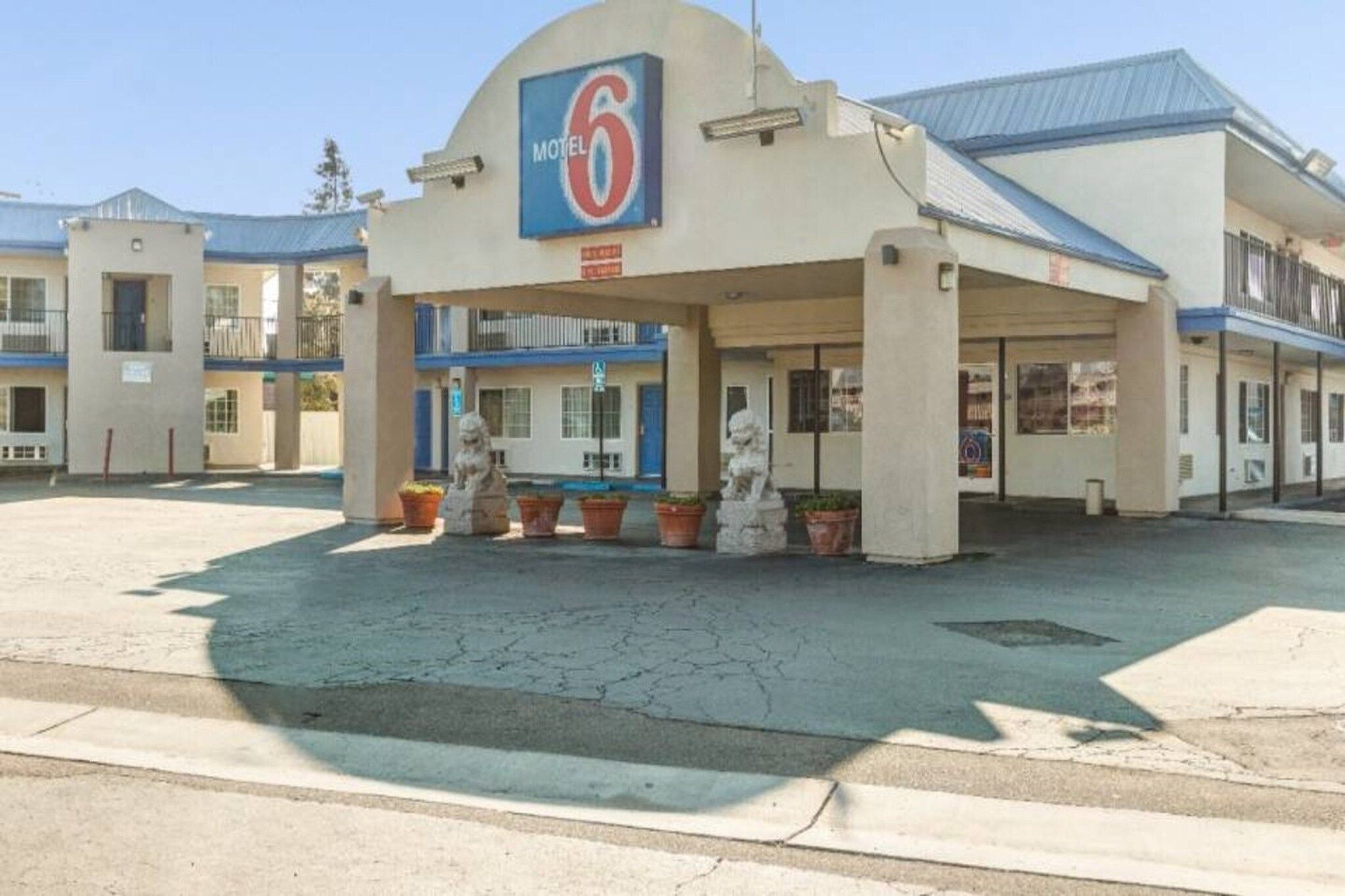Ein Motel mit einem auffälligen Schild mit der Zahl 6, einem überdachten Parkbereich und einer Reihe von Blumentöpfen.