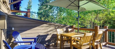 Een houten terras met een tafel, stoelen en een parasol, met uitzicht op bomen.