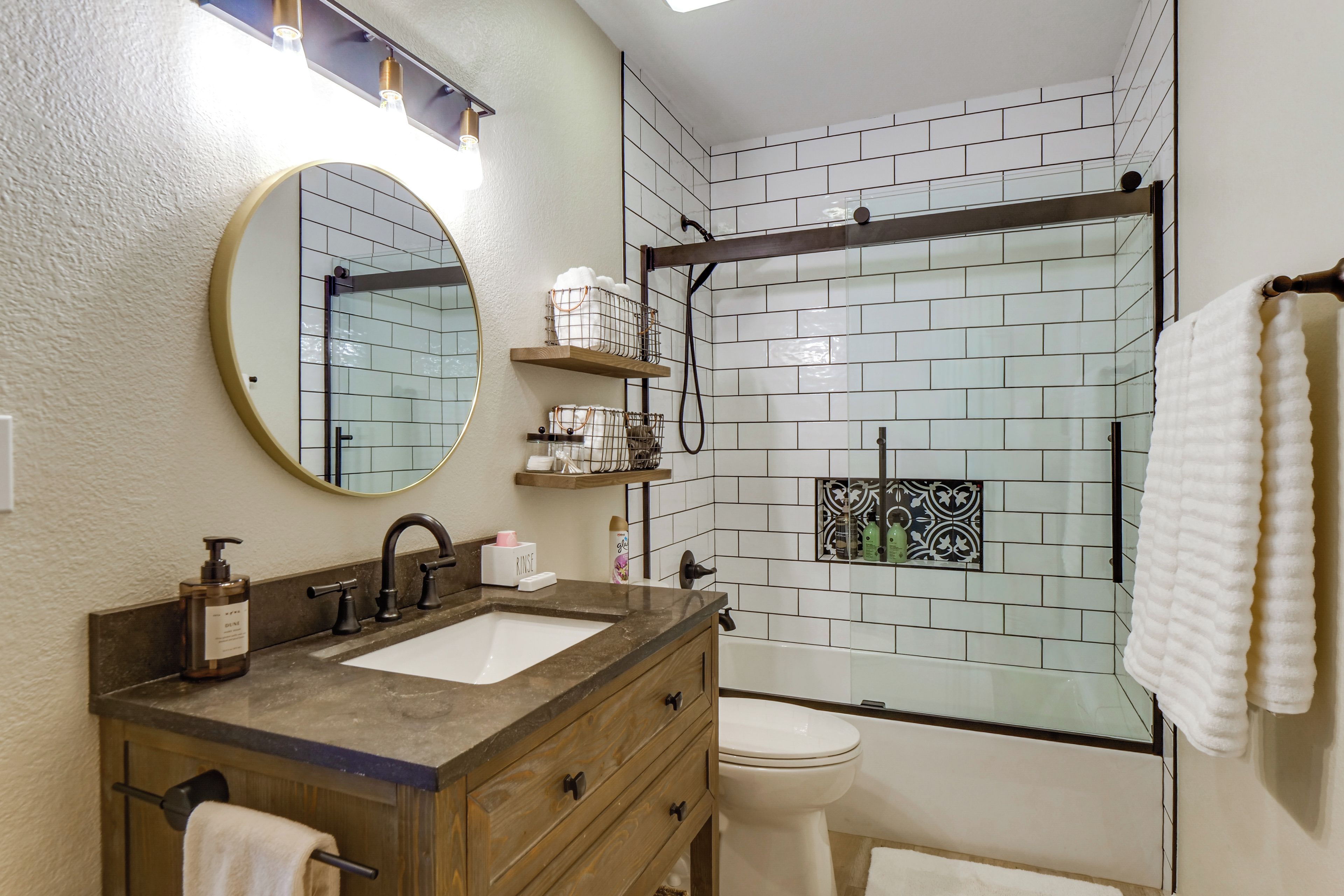 Een badkamer met een wastafel, spiegel, wastafelmeubel, handdoekrek, douche en toilet.