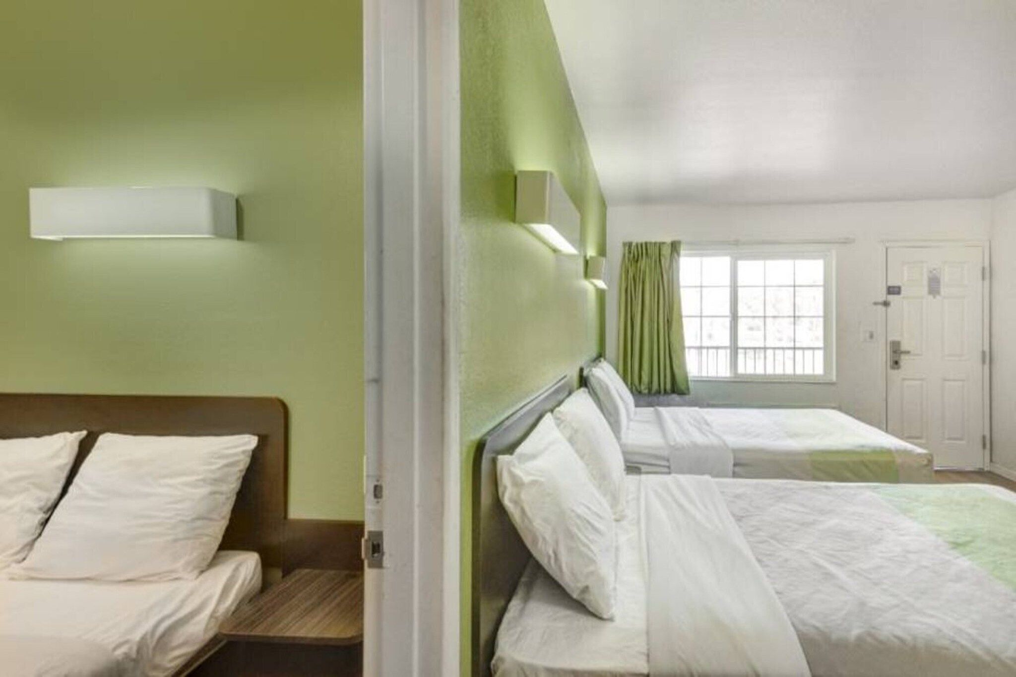 Ein Hotelzimmer mit zwei Betten, einem Fenster mit Vorhängen und einer Tür.