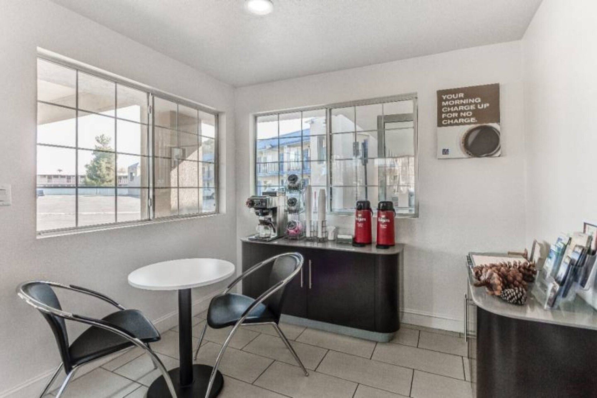 A small room with a white table and two chairs, a coffee machine, and a sign on the wall.