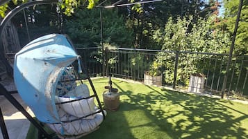 Een tuin met kunstgras, een schommel en een pergola.
