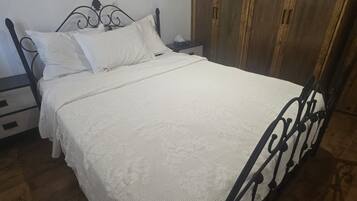 Un letto singolo con struttura in metallo e biancheria da letto bianca, un armadio in legno e un comodino con una lampada.