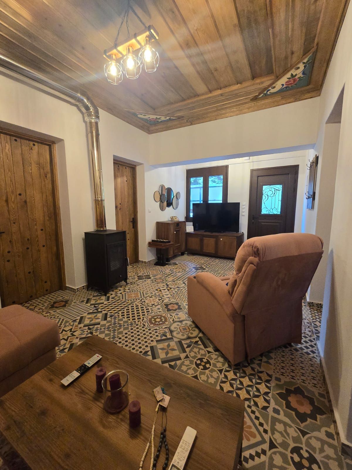 A living room with a patterned floor, a television, a sofa, and a wooden ceiling.