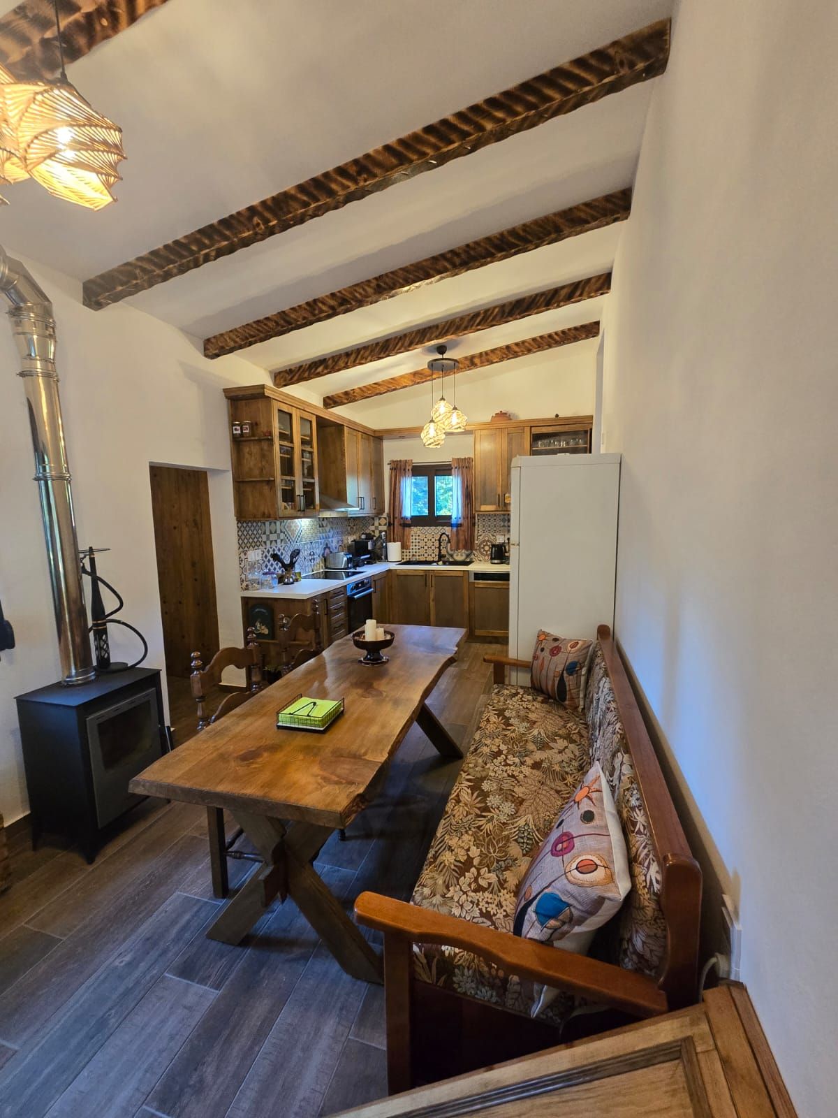 Un interno accogliente con tavolo da pranzo in legno, sedute tipo panchina, angolo cottura e un camino a vista.