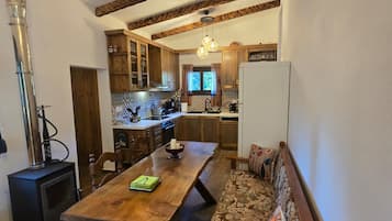 Un interno accogliente con tavolo da pranzo in legno, sedute tipo panchina, angolo cottura e un camino a vista.