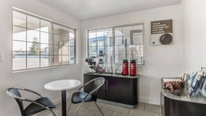 Une petite pièce avec une table blanche et deux chaises, une machine à café et un panneau accroché au mur.