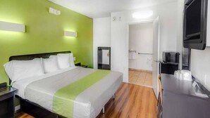 Une chambre d’hôtel avec un lit, des tables de chevet, un téléviseur et une salle de bain visible à travers une porte ouverte.