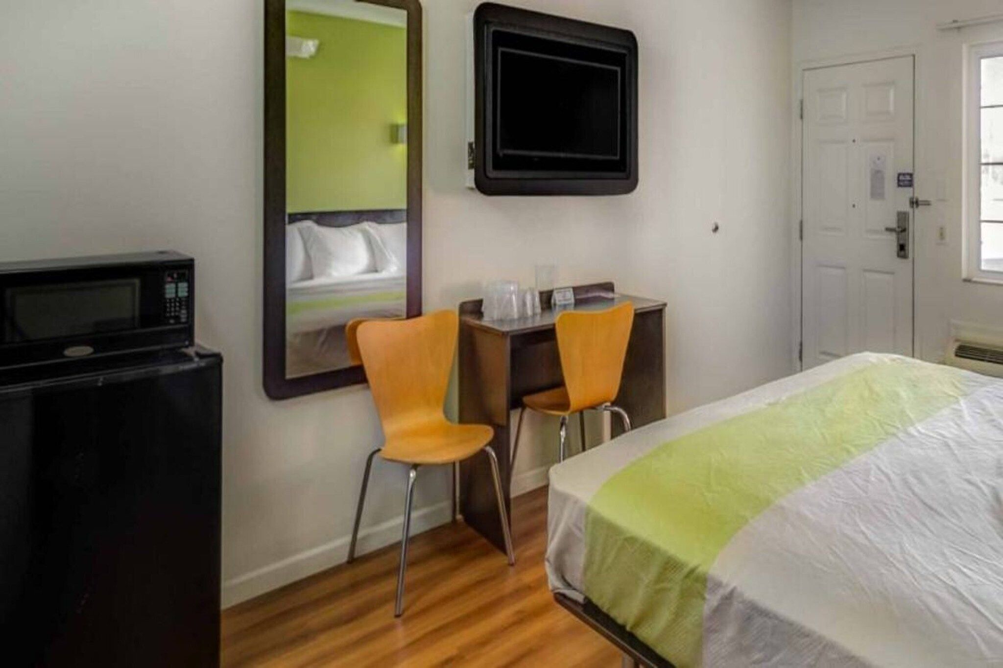 A hotel room with a bed, a desk, two chairs, a microwave, a mirror, and a television.