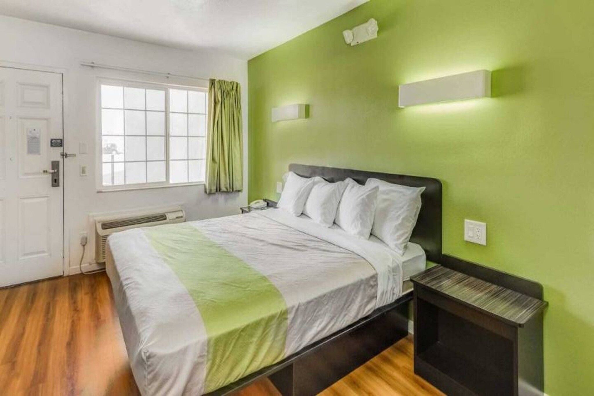Ein Schlafzimmer mit einem Bett, einem Nachttisch, einem Fenster mit Vorhängen und einer Wandleuchte.